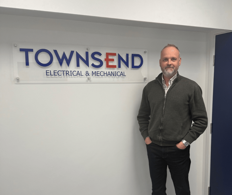 Paul Huntley standing in from of the indoors Townsend sign. Blue box: Townsend joins employer partner programme! TEC Partnership logo top left Townsen